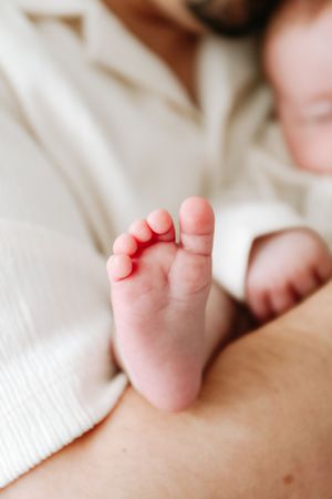 Tiny pink baby feet showing closeup details of soft newborn toes against white bedding.