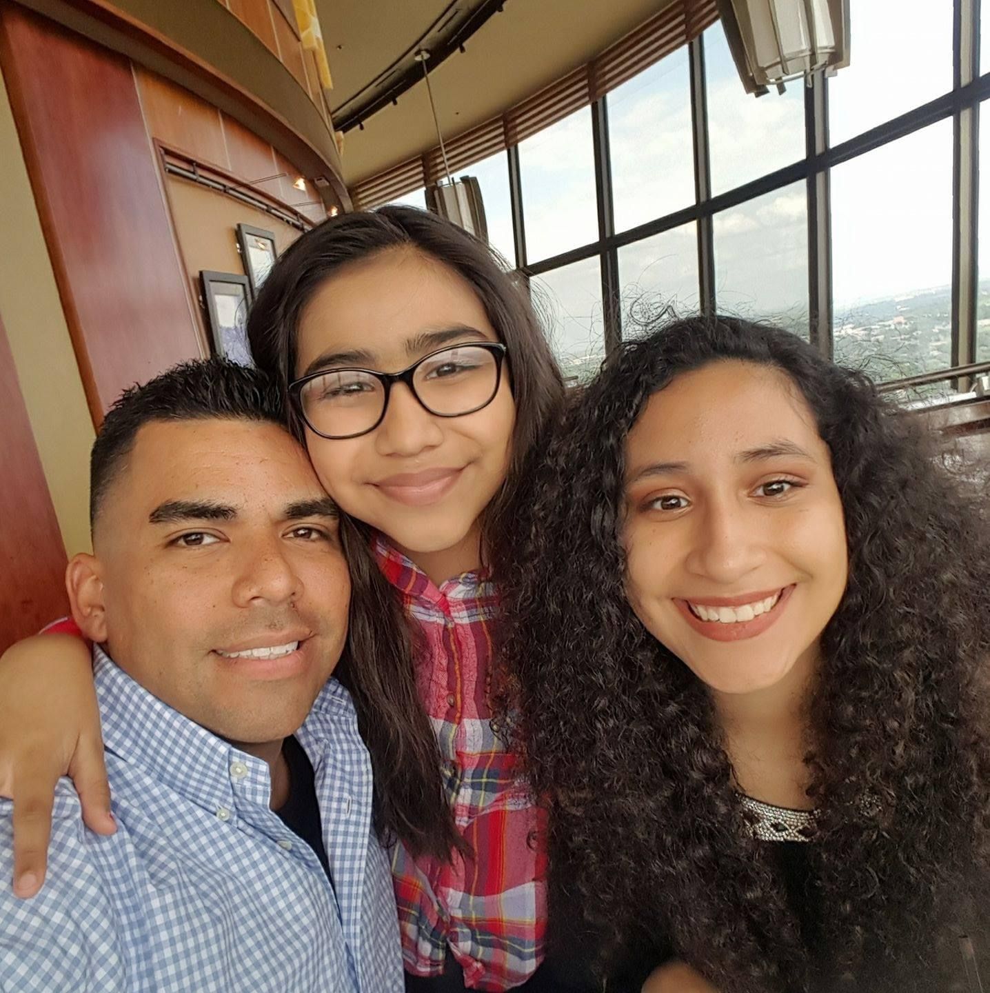 Three people smiling together in casual attire by window with city view.