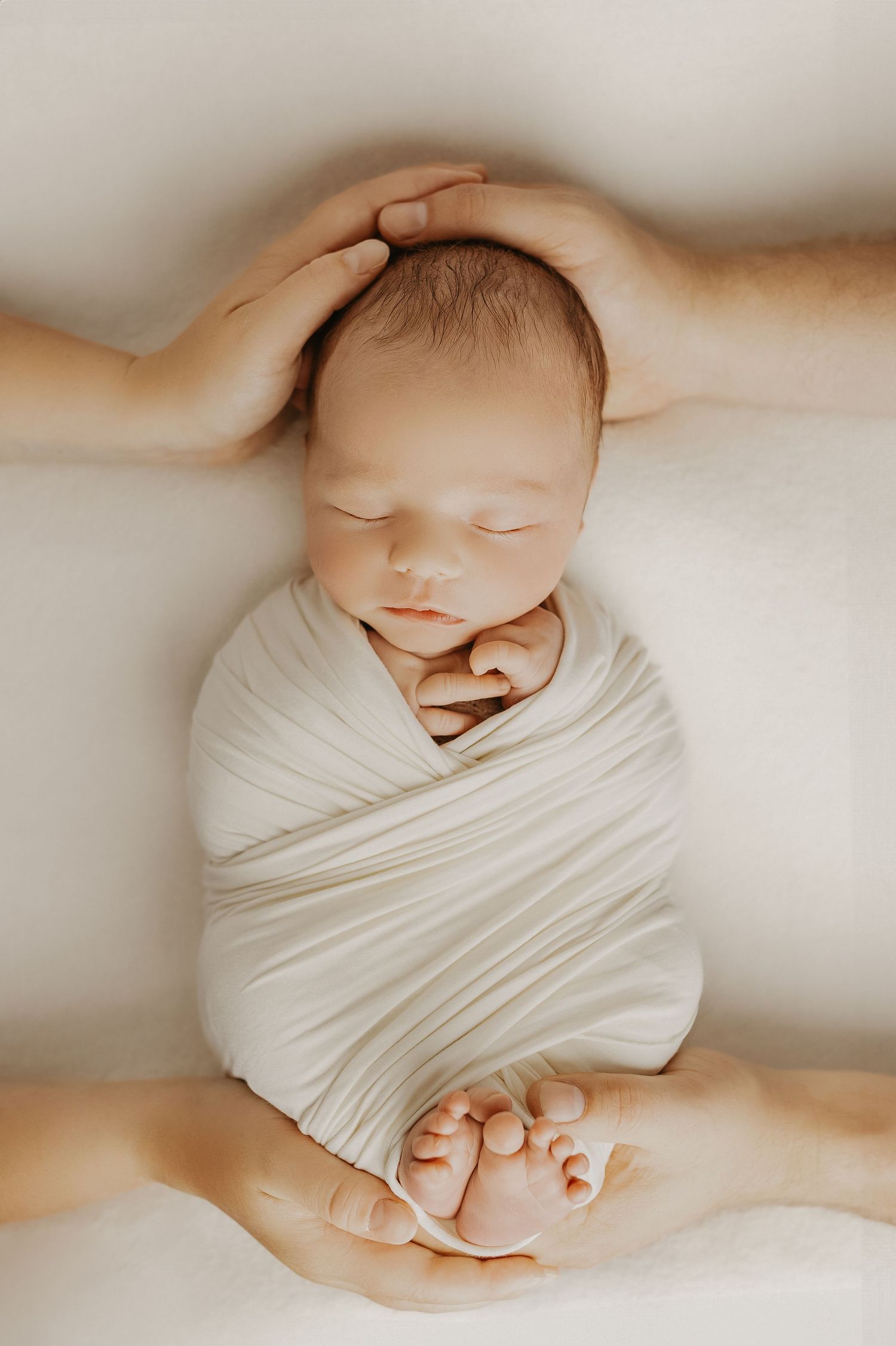 Minimalist newborn photography with baby wrapped in white fabric against neutral background.