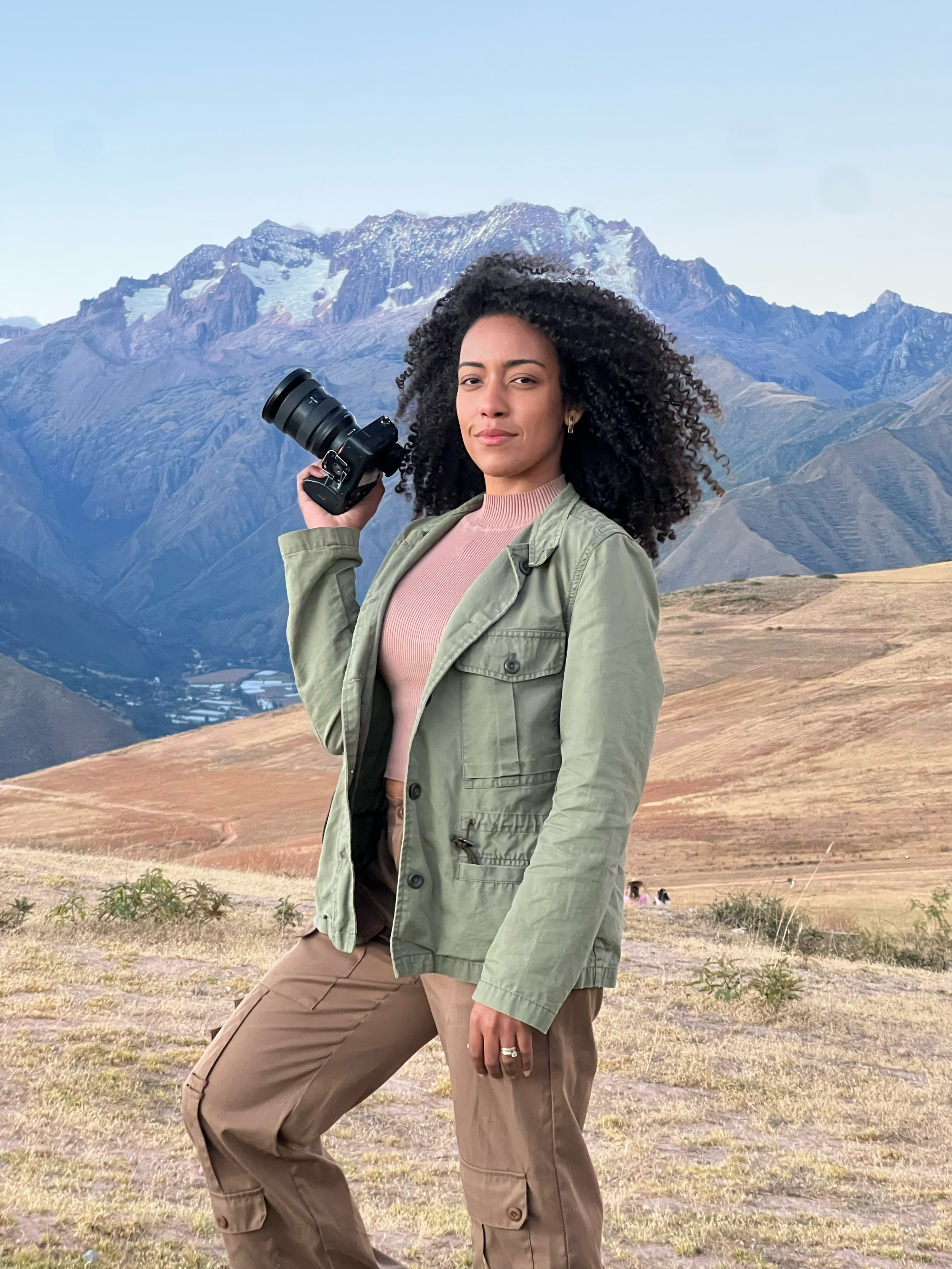 Adventure photography with mountains in background showing photographer in olive jacket and brown pants.