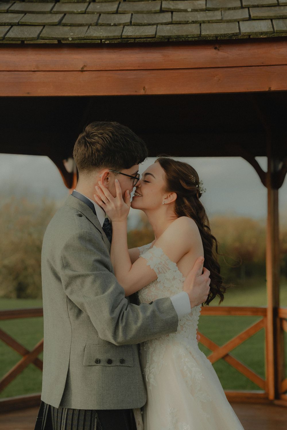 Bride and groom sharing a kiss under a wooden gazebo in soft golden light.