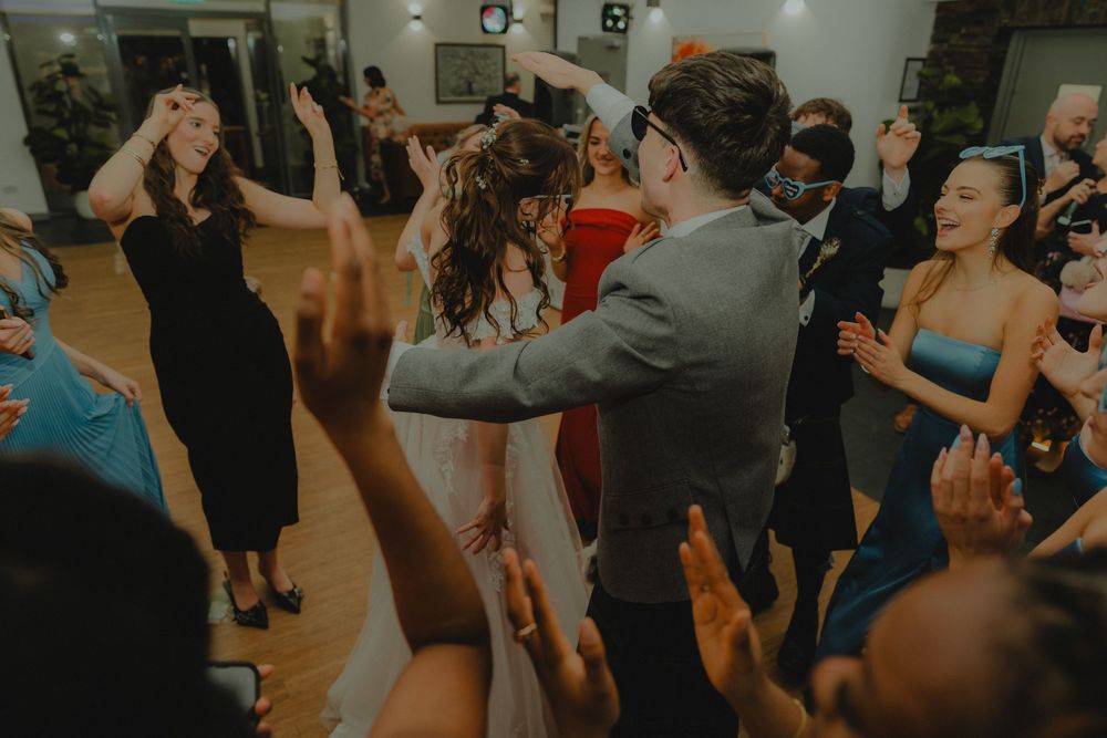 Bride and groom dancing joyfully with guests at a lively wedding reception party on the dance floor.