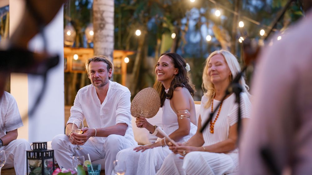 Friends enjoying drinks and conversation at an outdoor evening dinner party with twinkling lights overhead.