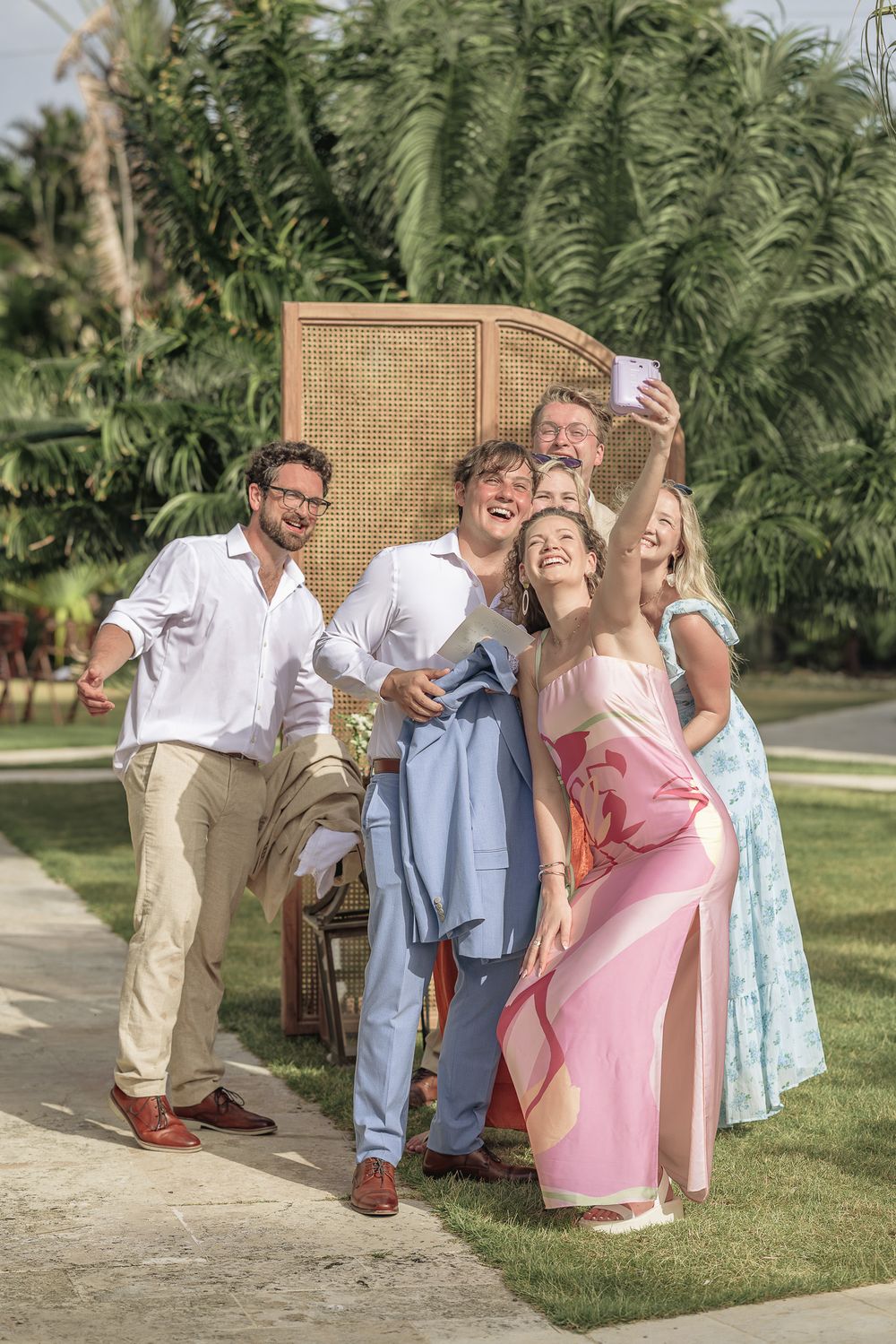 People in summer attire posing playfully on outdoor patio with lush greenery and wicker furniture.