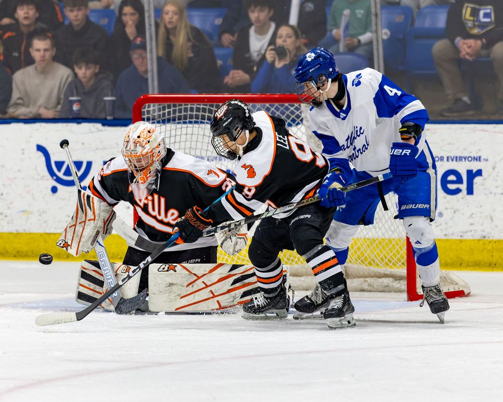A hockey game in progress, with players from opposing teams battling for the puck in front of the goal.