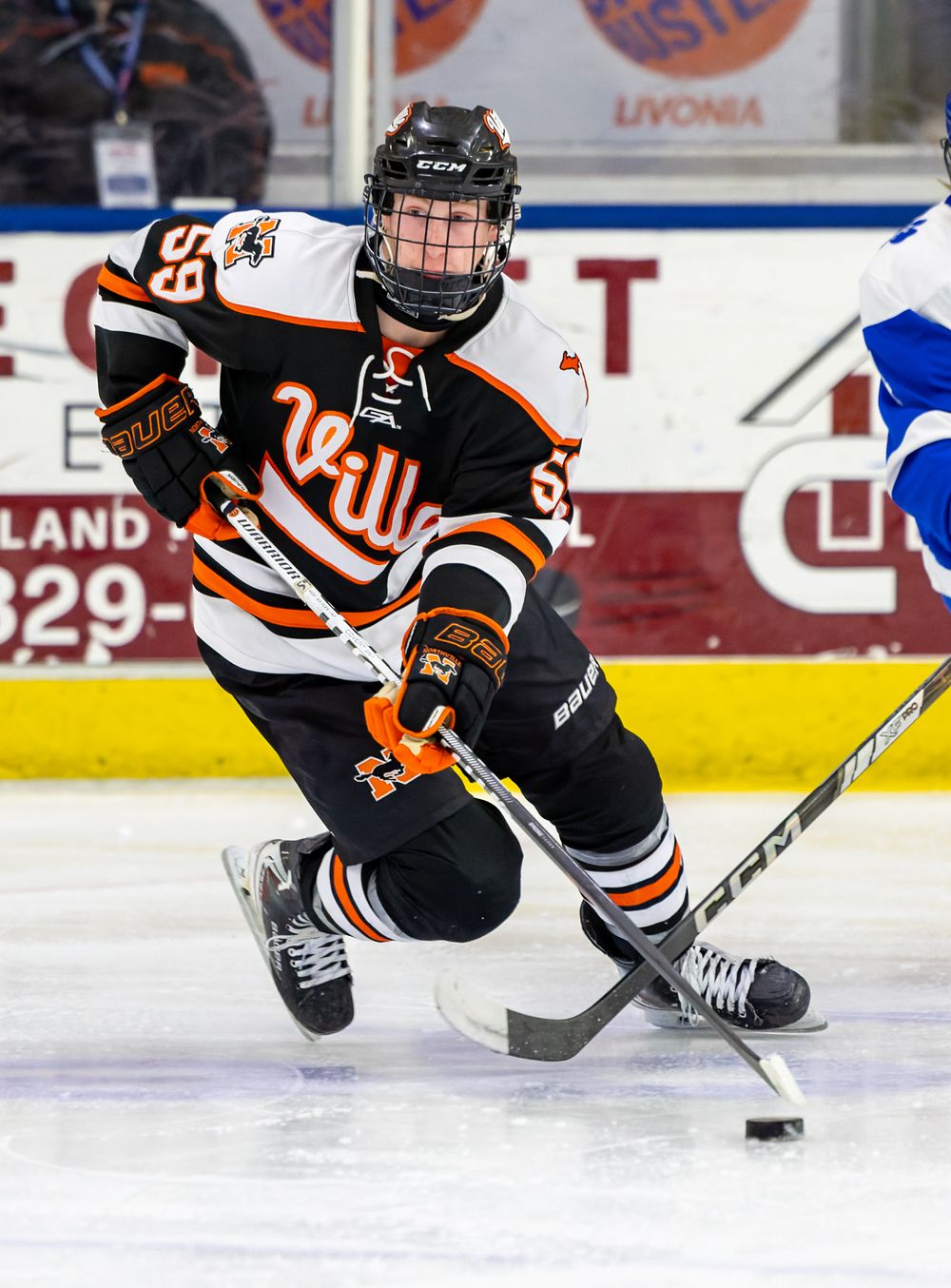 A hockey player in an orange and black jersey is skating on the ice while holding a hockey stick.