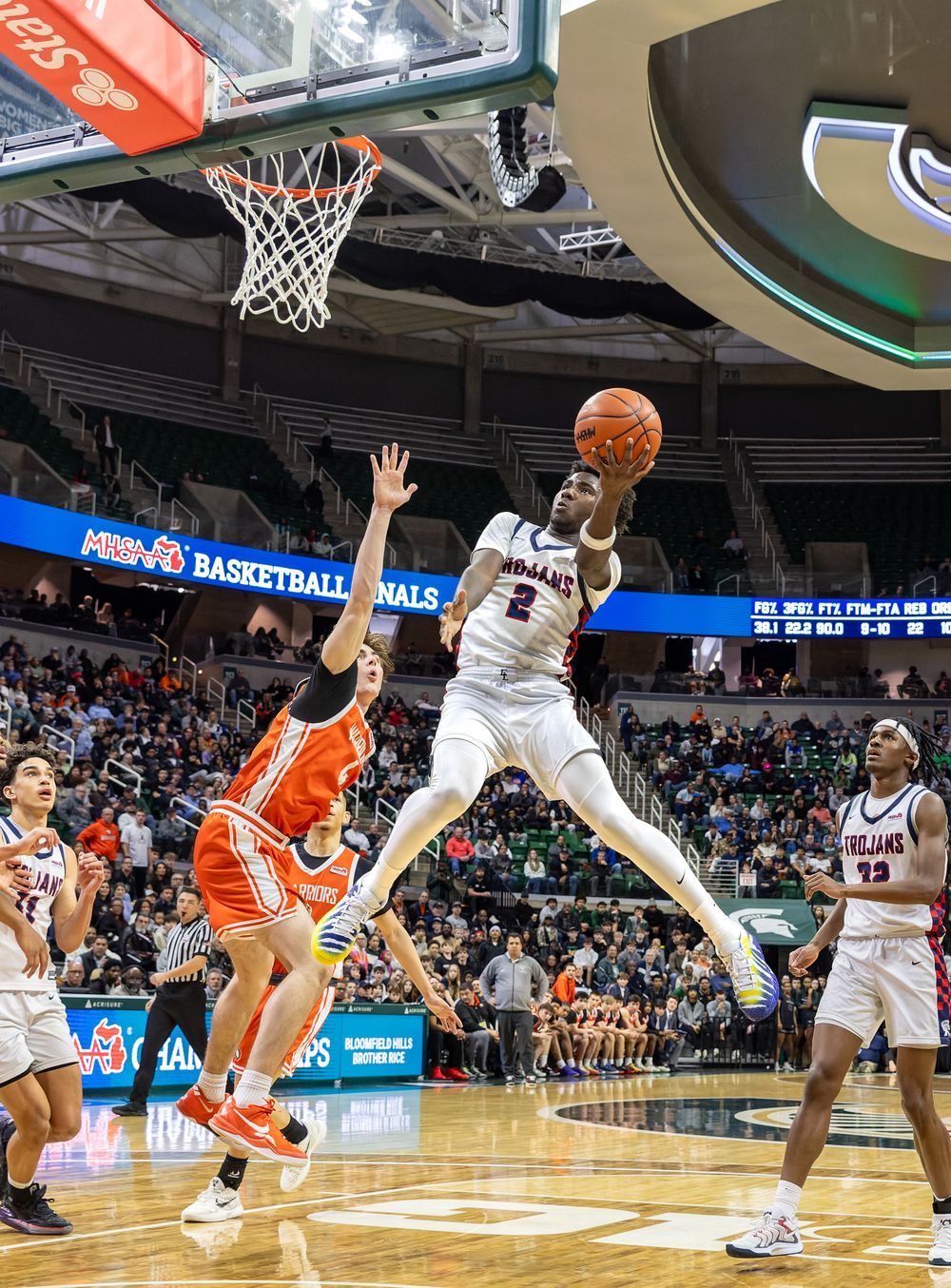 A basketball player jumps high to make a shot while another player tries to block the shot.