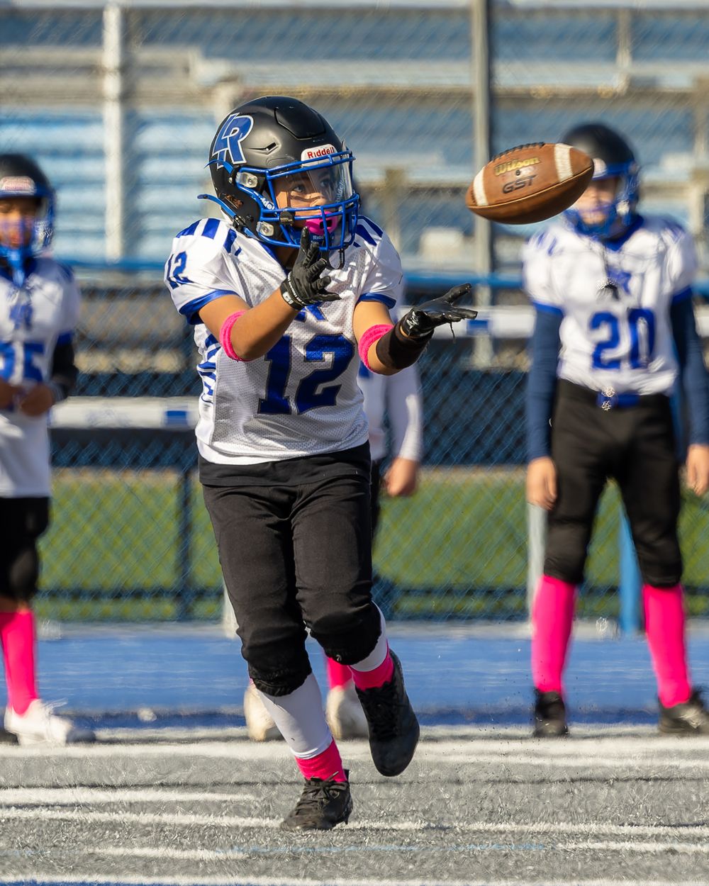 Football player in black uniform and pink socks performs a diving catch during a game on artificial turf.