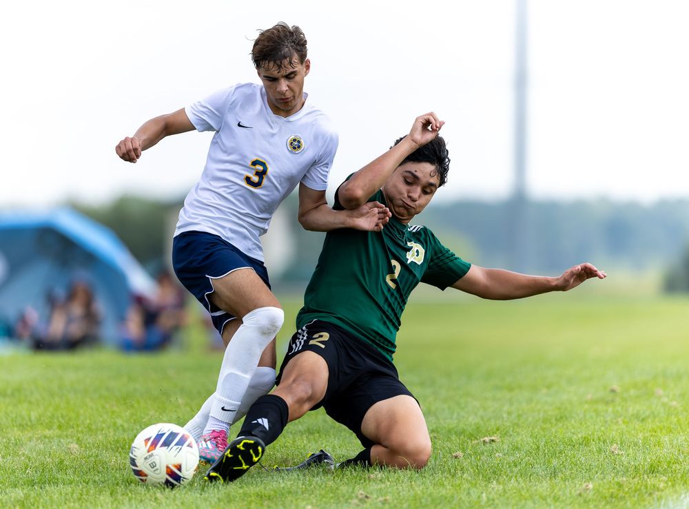 Soccer players slide tackle for the ball during an intense match on a grass field.