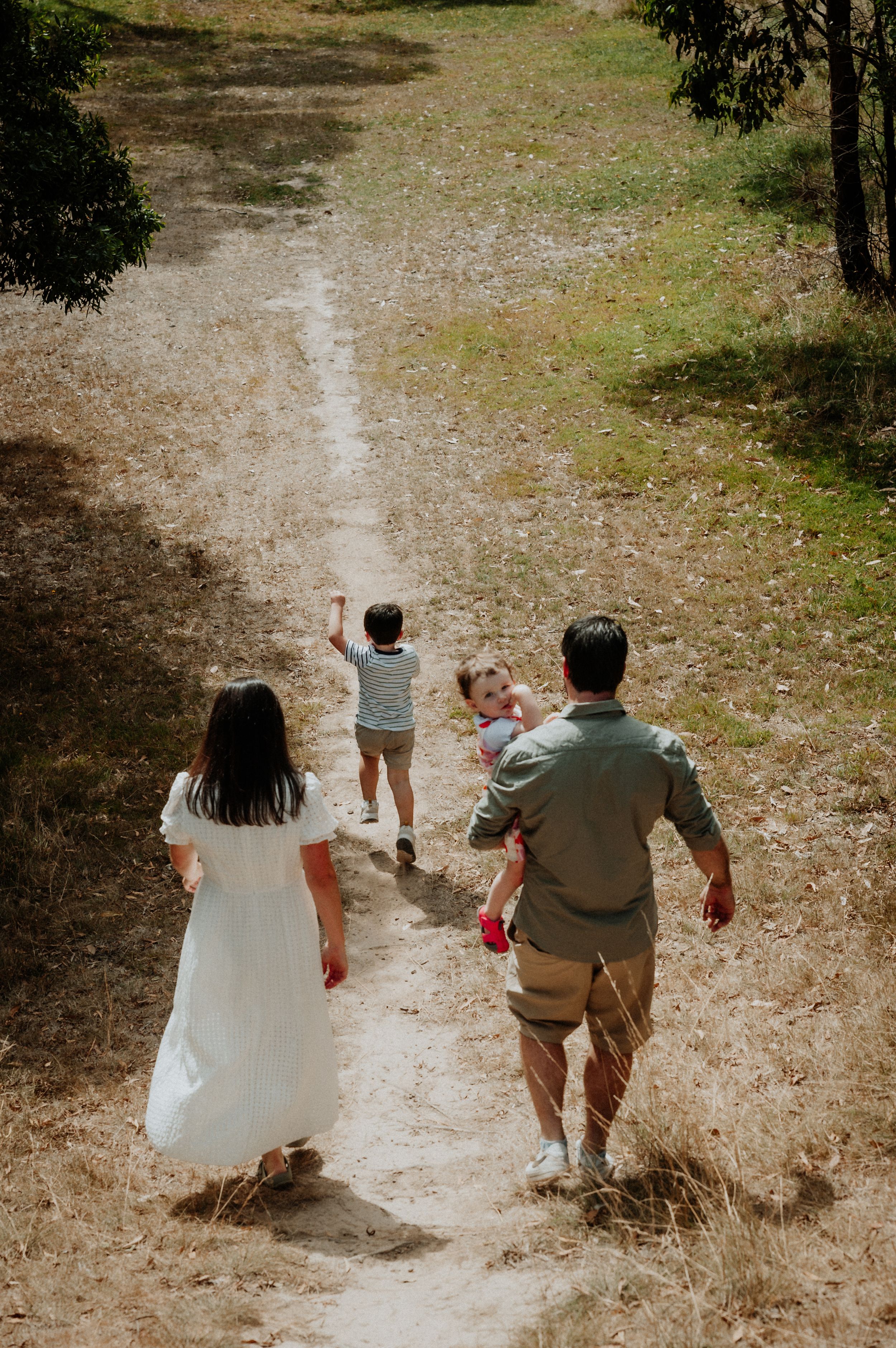 A family walks down a winding dirt path together in a eucalyptus grove on a sunny day.
Altona Family Photographer Melbourne