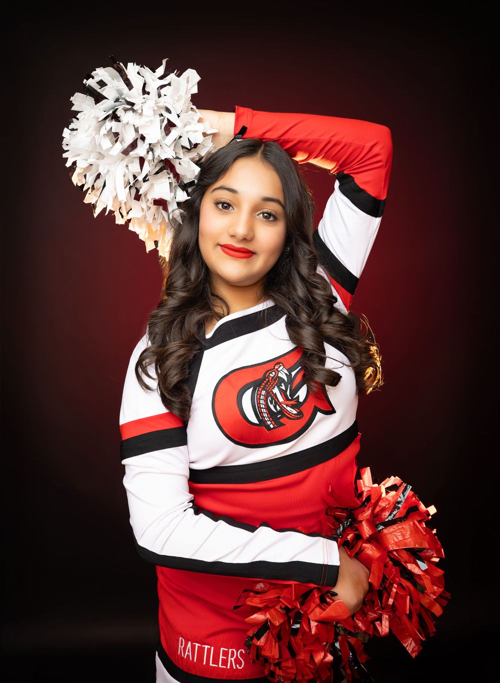 Cheerleader in red and white uniform holds pom pom overhead with confident smile.