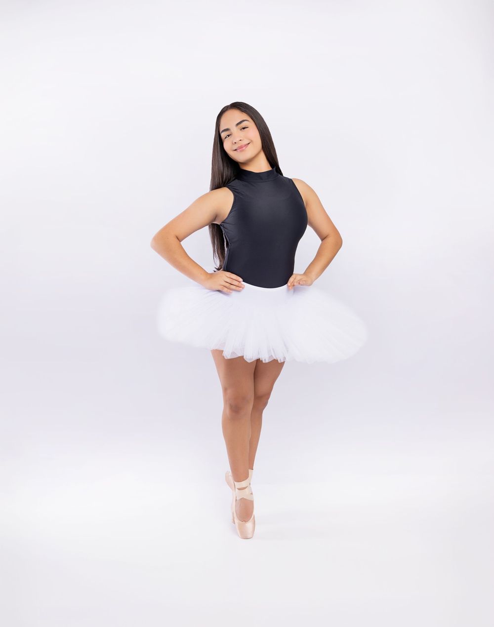 A ballet dancer in a black leotard and white tutu poses gracefully en pointe against a white background.
