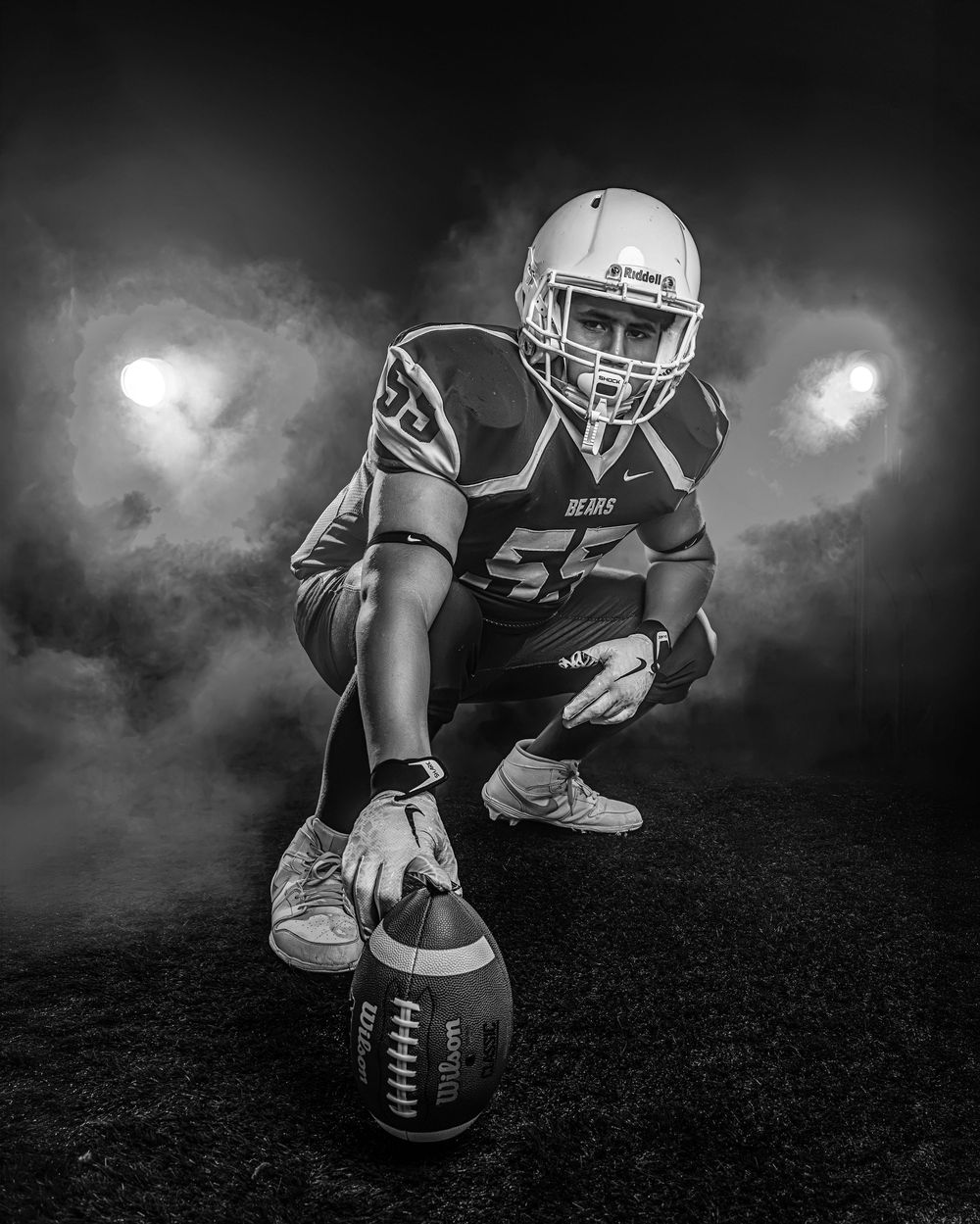 Black and white photo of a football player in Bears jersey number 55 crouching with a football on a smoky field.