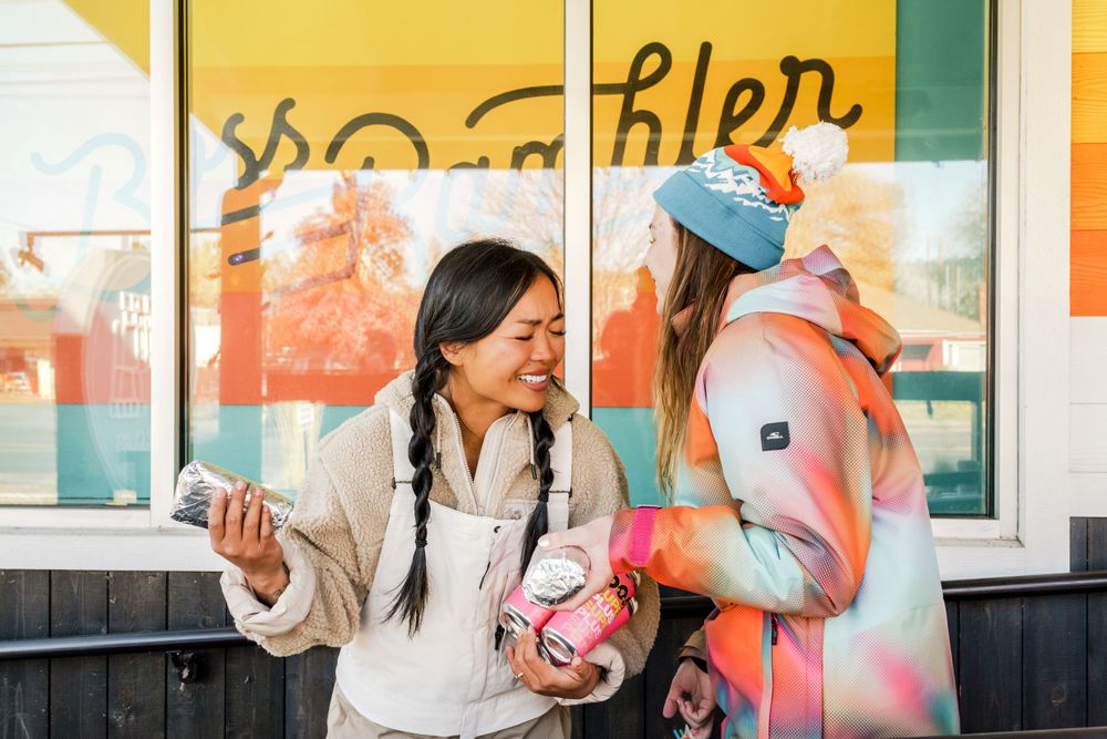 Friends enjoy refreshments together outside of a storefront window on a sunny day.