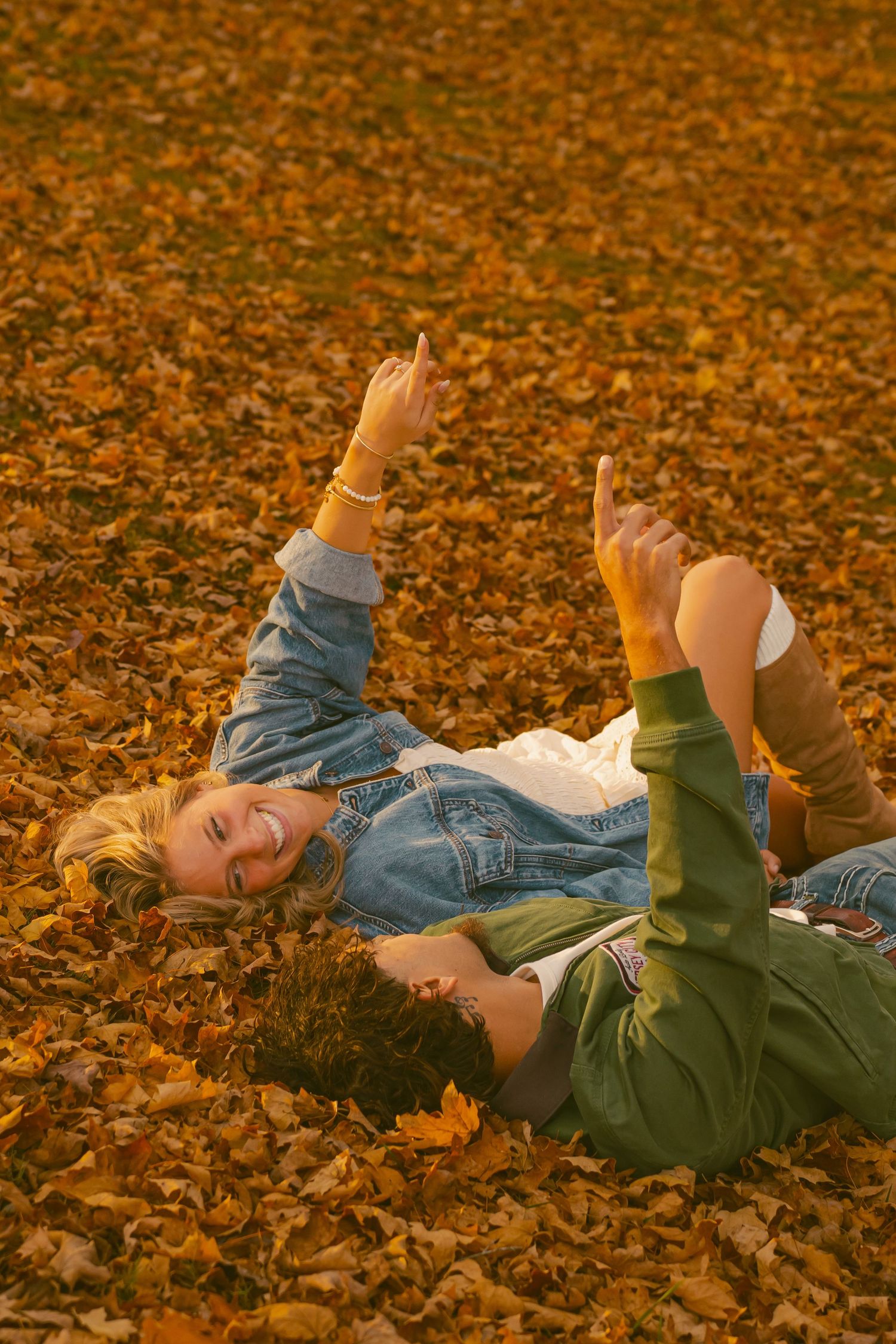 Person lying in pile of golden autumn leaves during sunset.