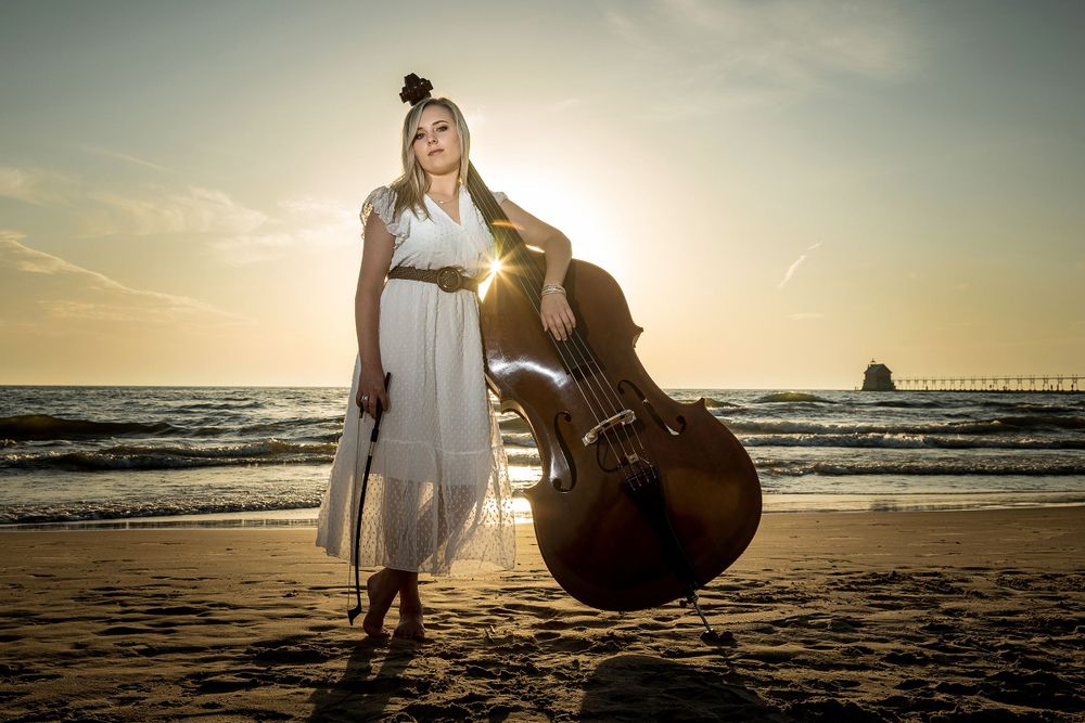 Musician with upright bass poses on beach during golden hour sunset. Grand Rapids Photographer