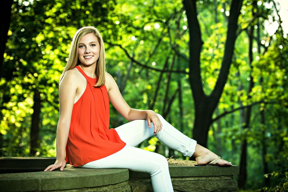 Summer outdoor portrait featuring a bright orange dress and white pants in a vibrant forest setting. Grand Rapids Photographer
