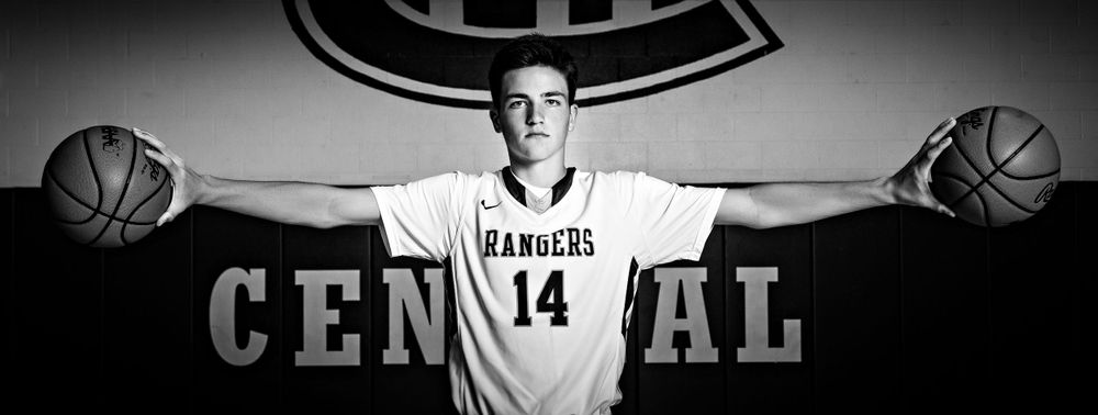 High school athlete poses with basketballs against Central team logo backdrop in black and white. Grand Rapids Photographer