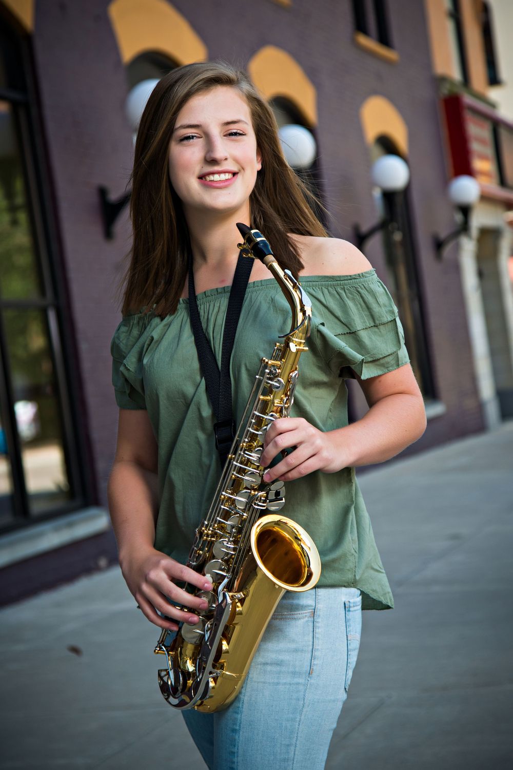 Musician in green off-shoulder top holding saxophone outdoors near storefront. Grand Rapids Photographer