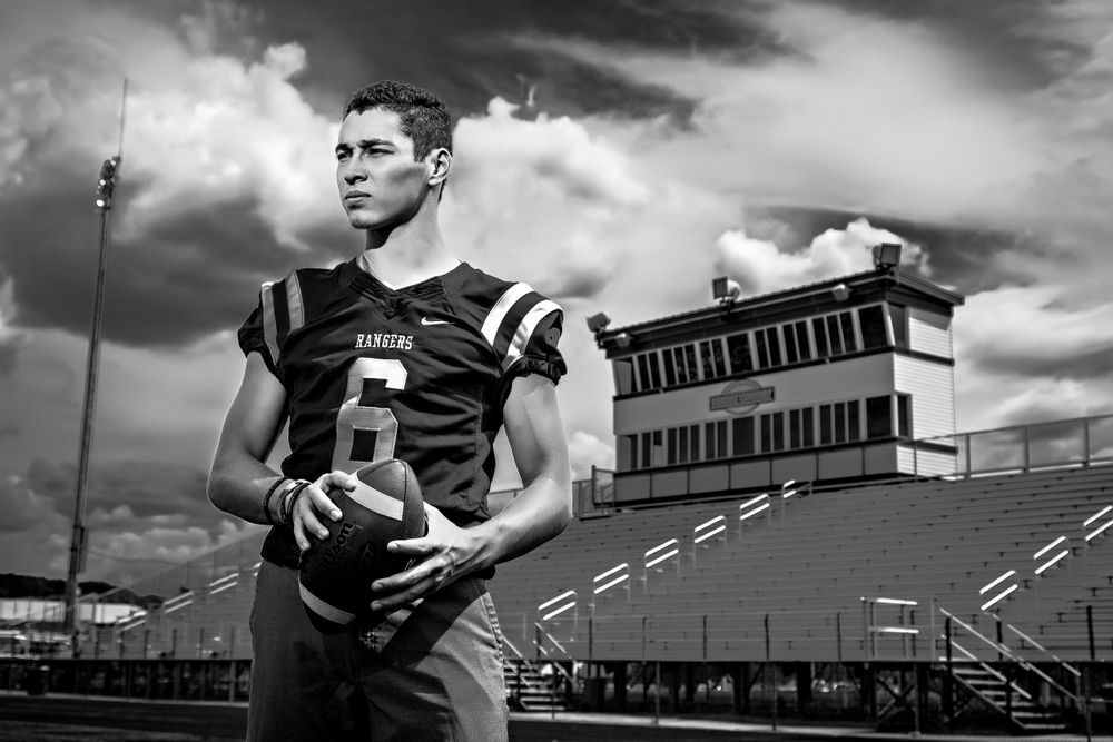 Black and white portrait of football player holding ball with stadium building in background. Grand Rapids Photographer