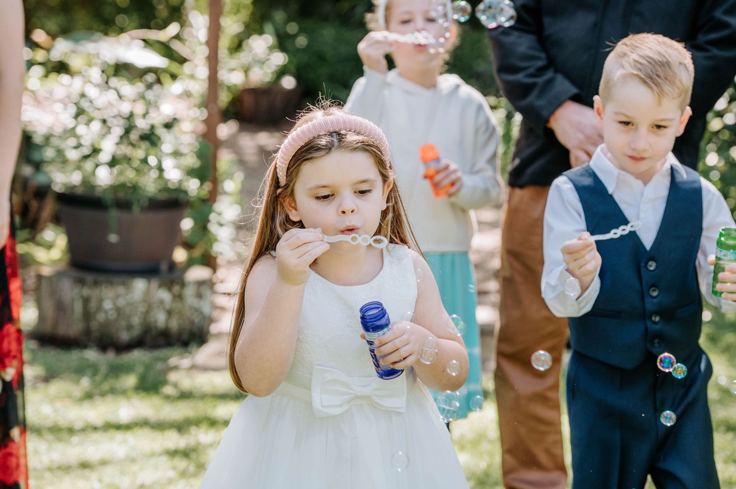 Children in formal attire playing with bubbles at an outdoor celebration.
