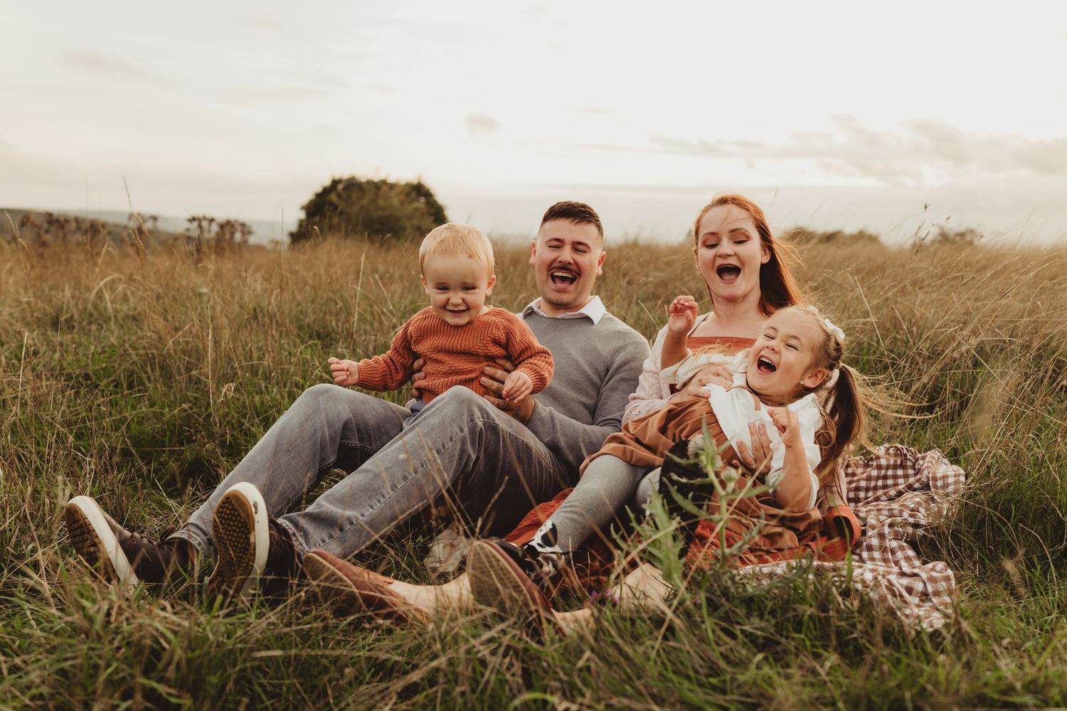 Family sitting together and enjoying each other's company in a grassy field during golden hour sunset.