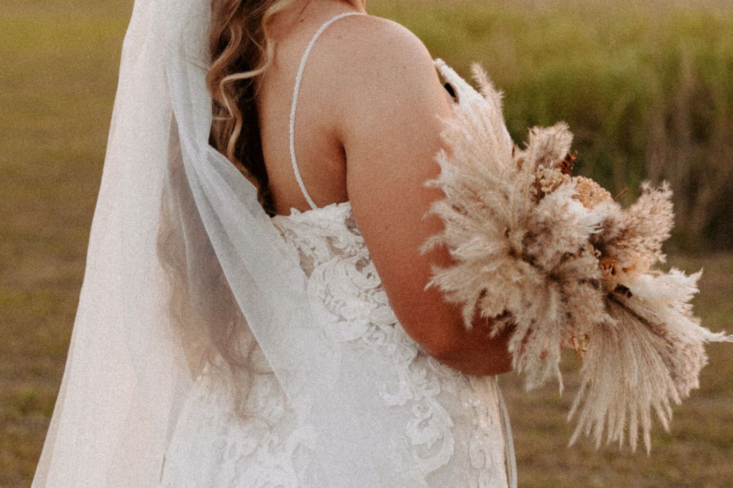 Bride in lace wedding dress holding a boho-style dried floral bouquet during golden hour. Oklahoma Wedding Photographer