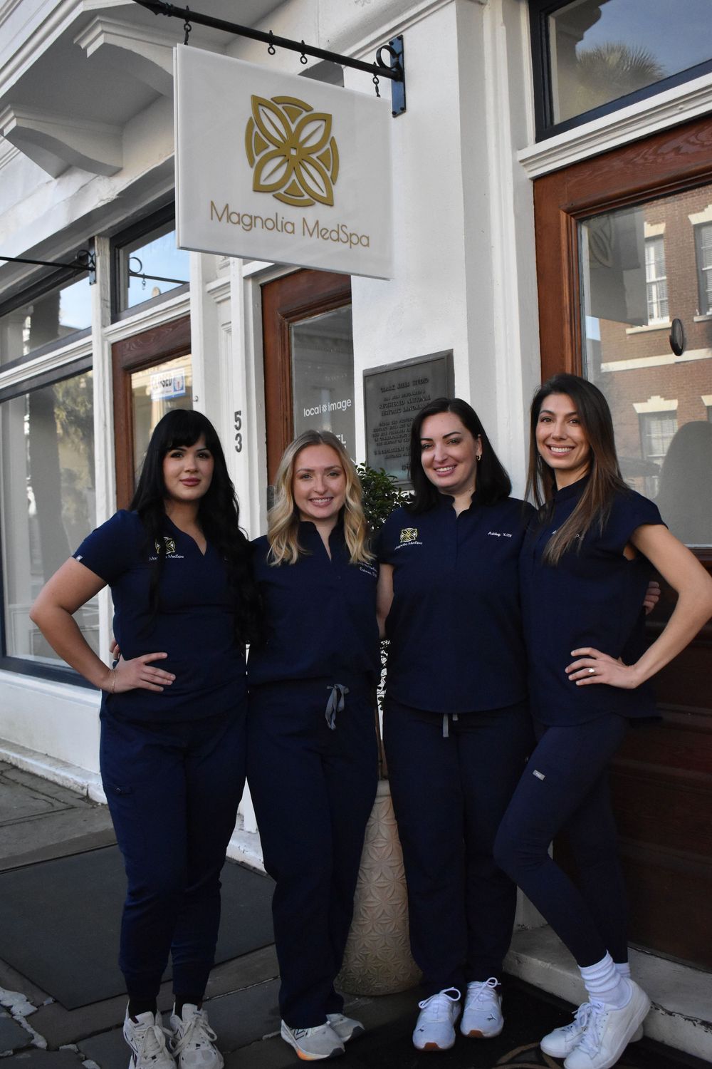 Medical staff in navy blue scrubs and white shoes pose together outside a healthcare facility entrance.