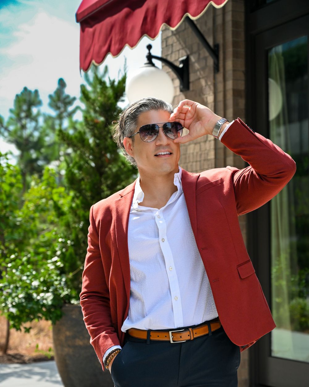 Professional wearing a burgundy blazer, white shirt and sunglasses poses confidently against an outdoor business setting.