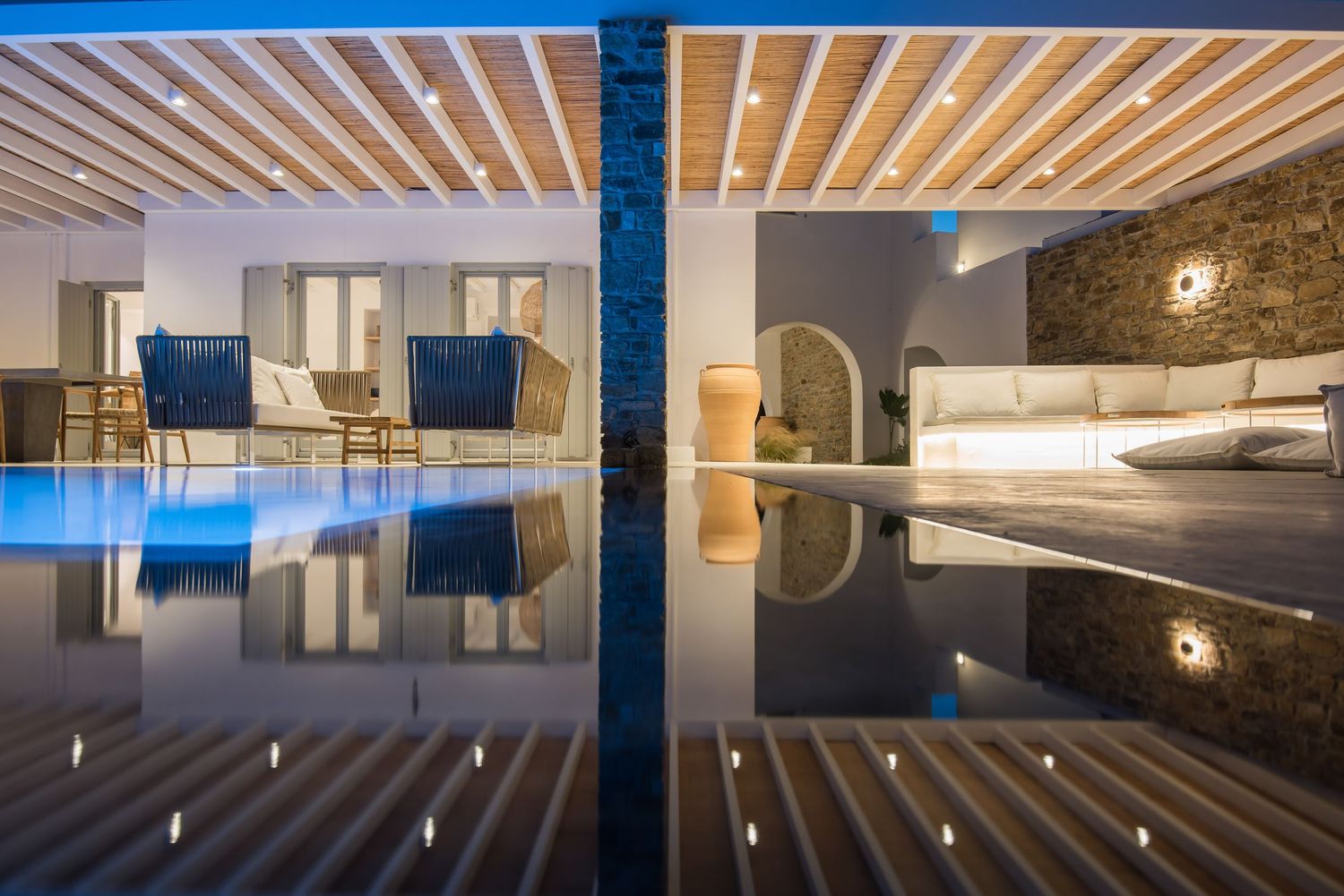 Elegant indoor pool with wooden ceiling beams and stone walls reflecting in still water at a luxury resort spa.