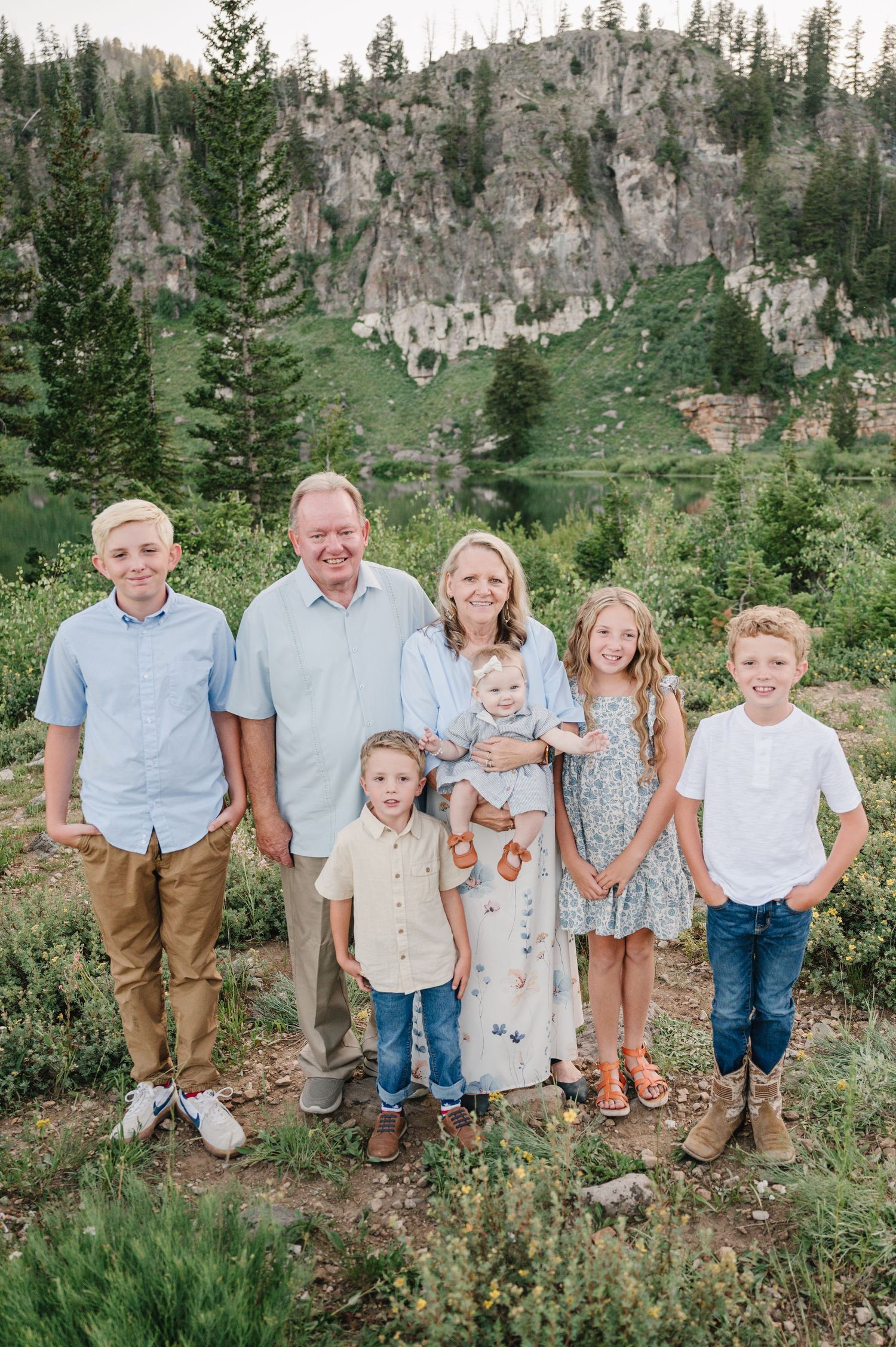 A group stands together against a scenic mountain backdrop with evergreen trees and rocky cliffs in Utah's wilderness.