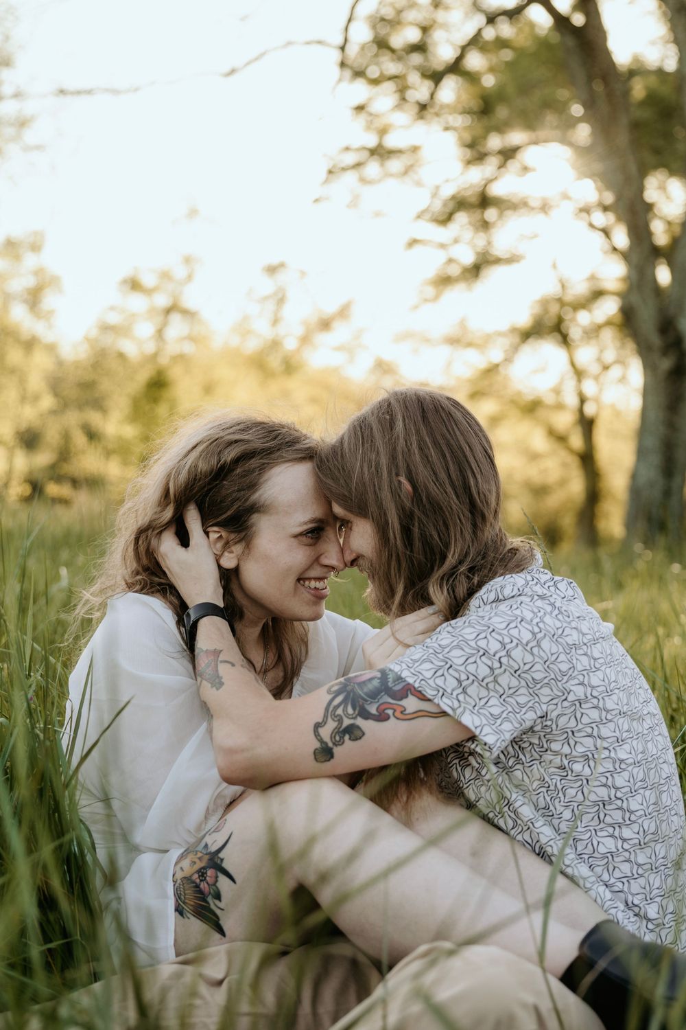 Couple sharing joyful laughter while embracing in tall grass during sunset.