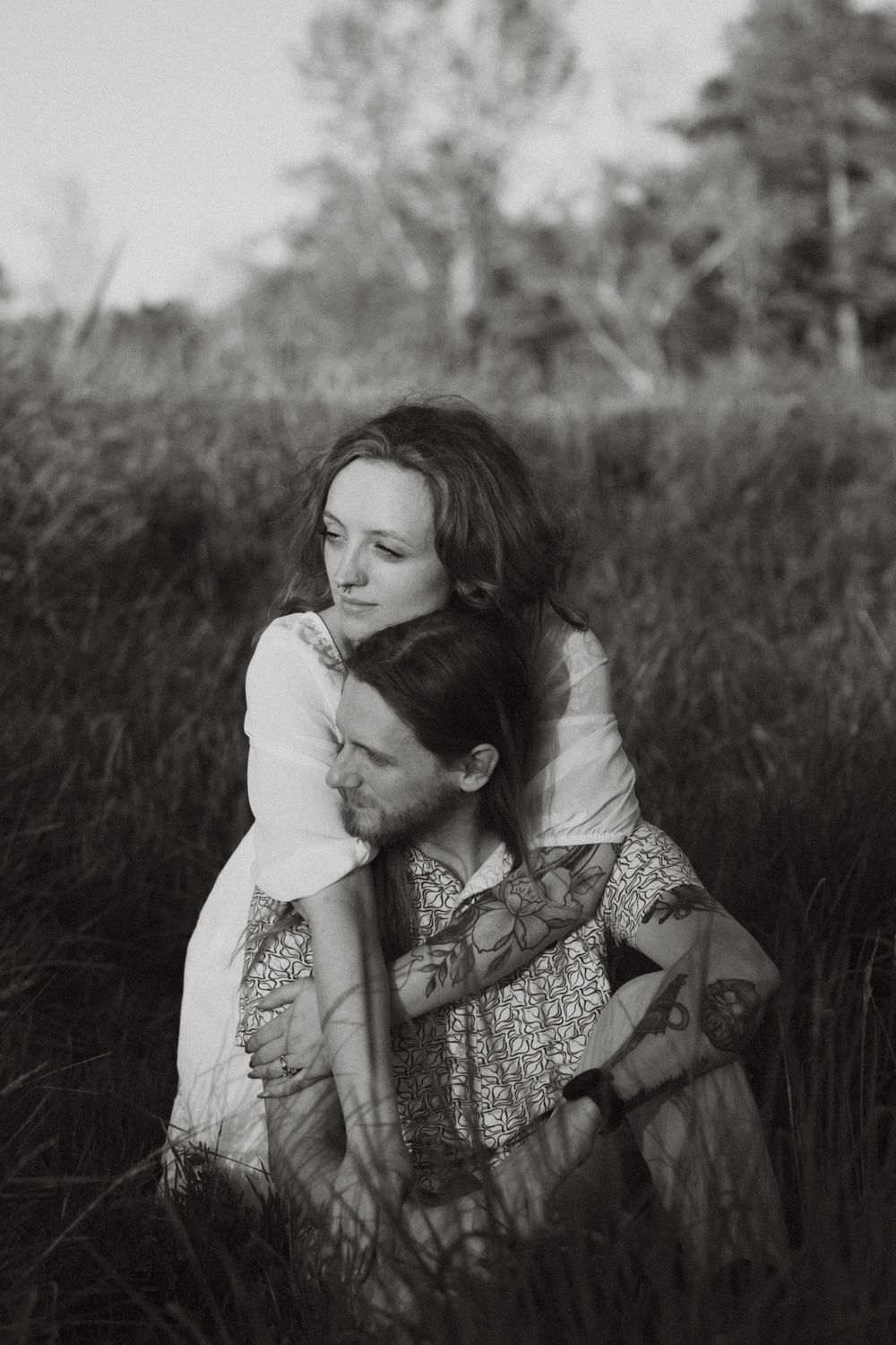 Black and white portrait of two people sharing an intimate embrace in a field of tall grass.