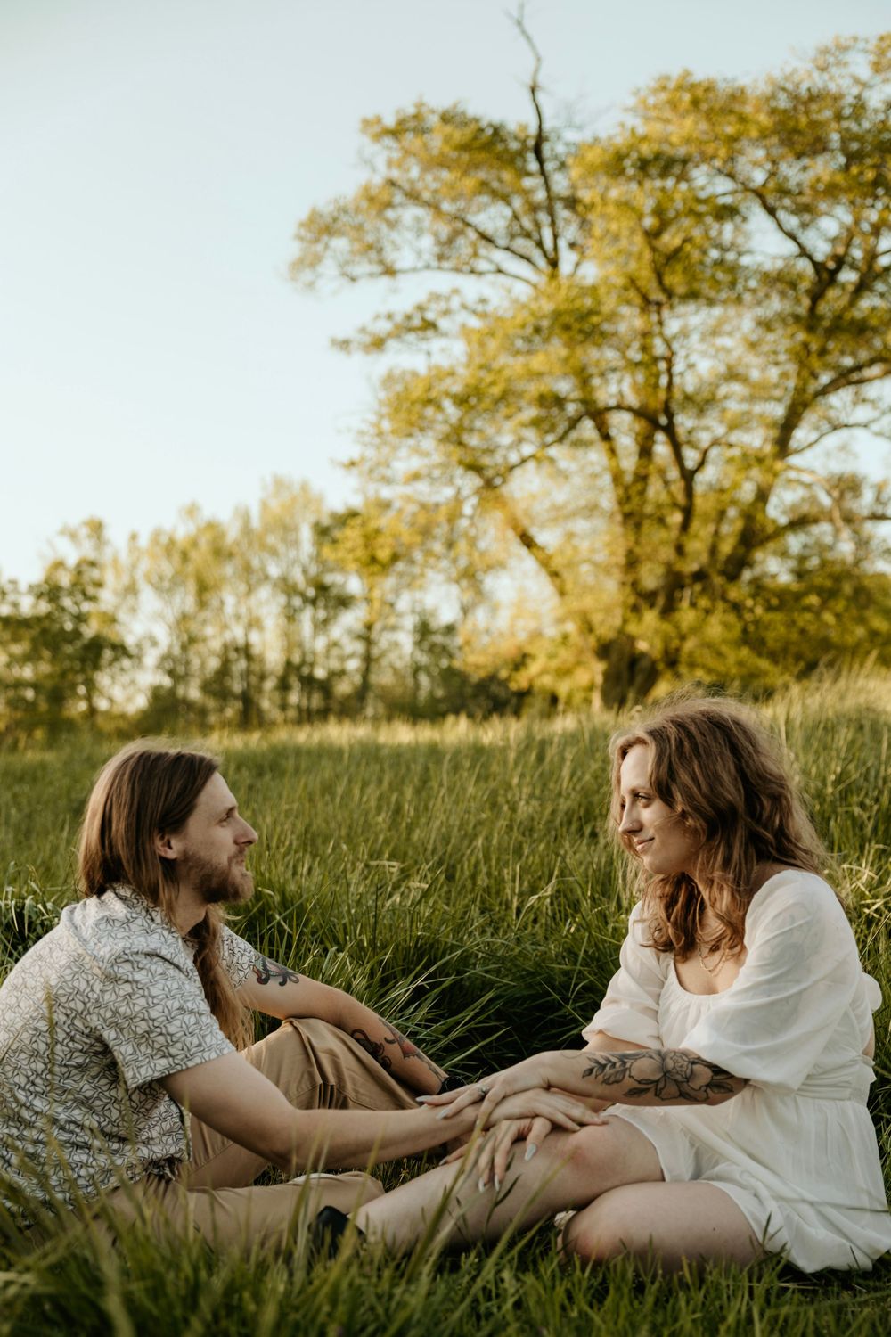 Couple sitting together in a sunlit meadow having an intimate conversation at golden hour.