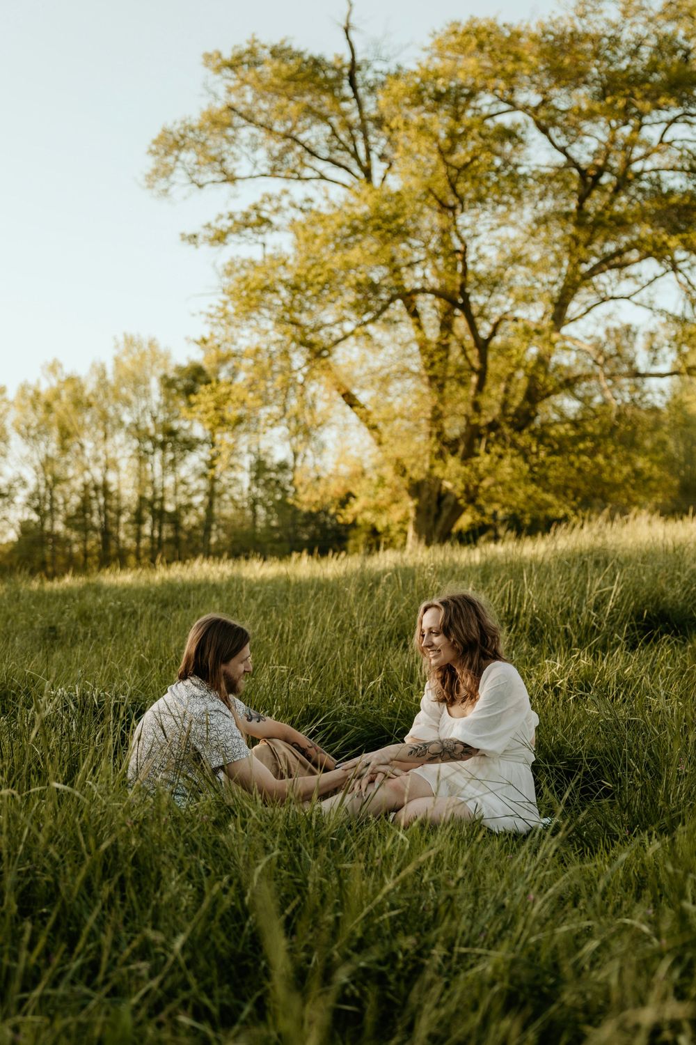 Two people sitting in conversation on a grassy hillside during sunset.