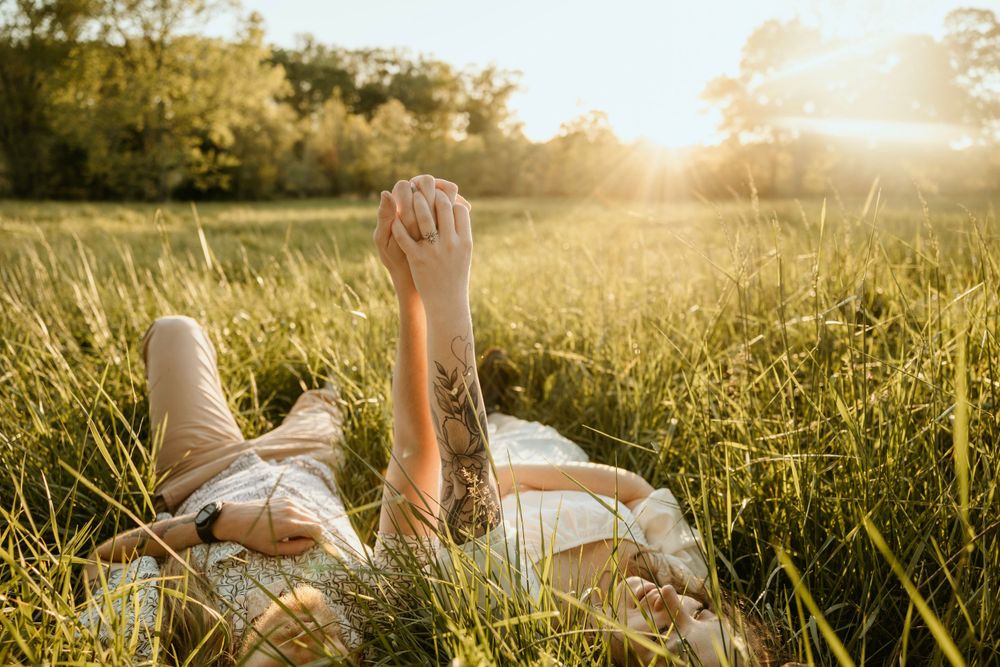 Person lying in tall grass at sunset with raised hand against the sunlit sky.