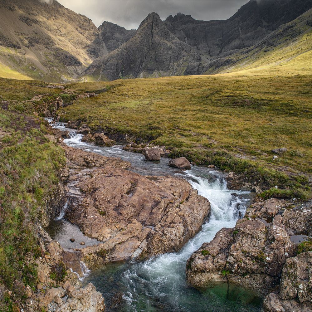Mountain stream cascading over rocky terrain with rugged peaks in the background.