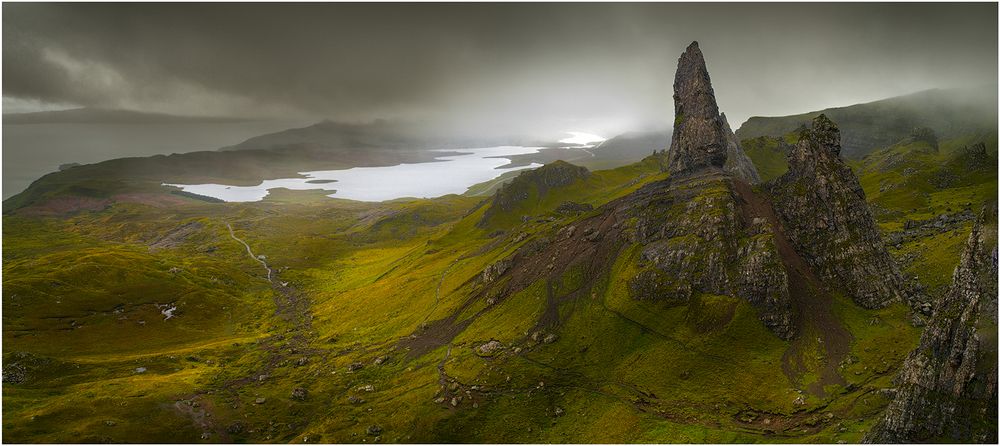 Dramatic panoramic view of misty Scottish highlands with rocky peaks and coastline.