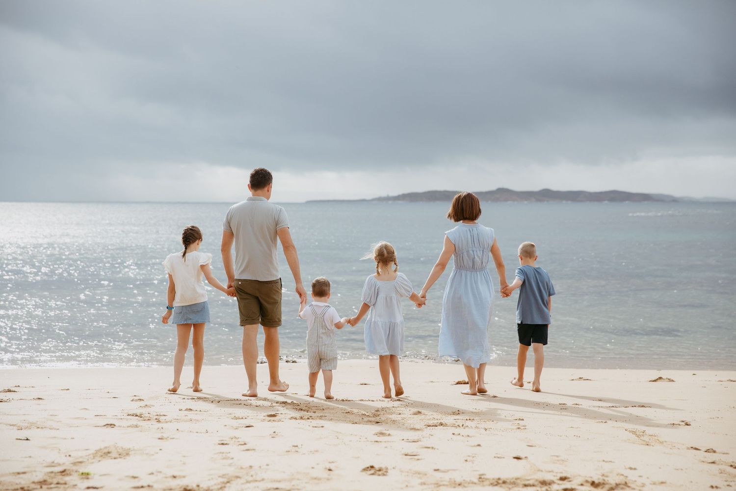A group of people stand together holding hands while looking out at the ocean on a cloudy day.