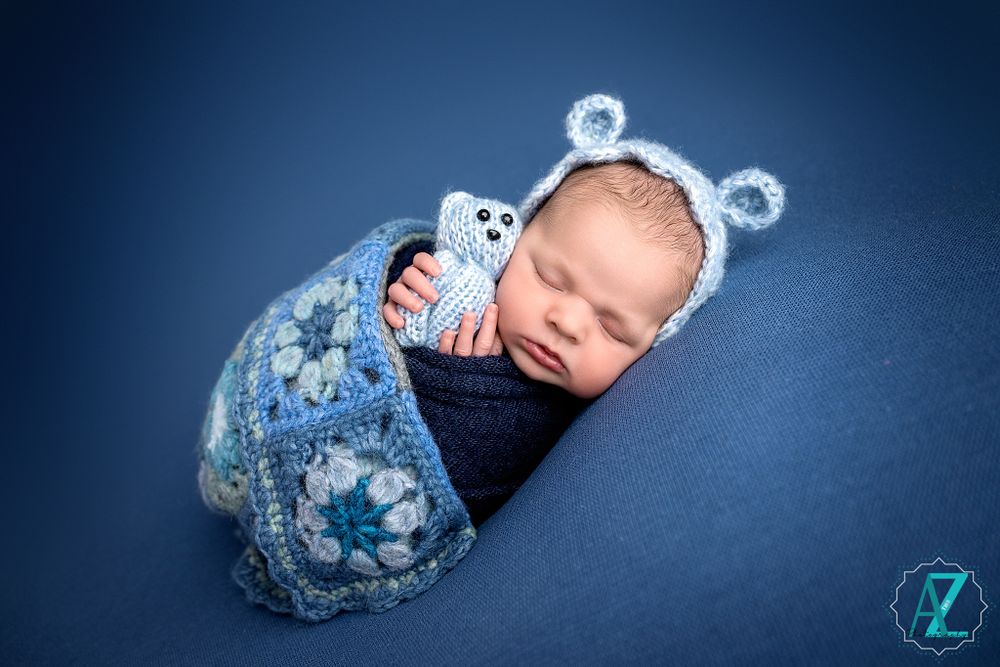 Sleeping baby in bear costume and navy wrap against blue background.