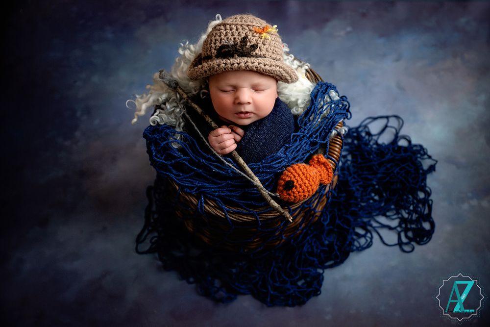 Newborn wearing knit hat nestled in dark blue blanket during professional photo session.