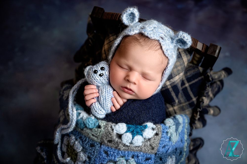 Sleeping baby wrapped in navy fabric with knit mouse bonnet and toy during studio portrait.
