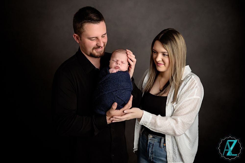 Family portrait with couple holding newborn against dark studio background.