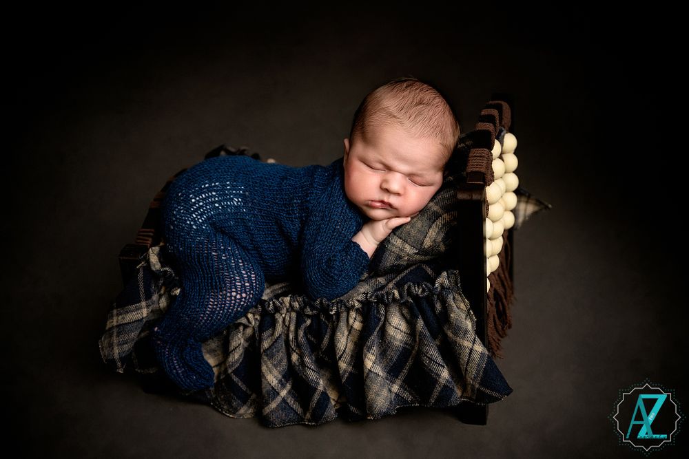 Sleeping newborn in navy wrap posed on plaid blanket during professional photo shoot.