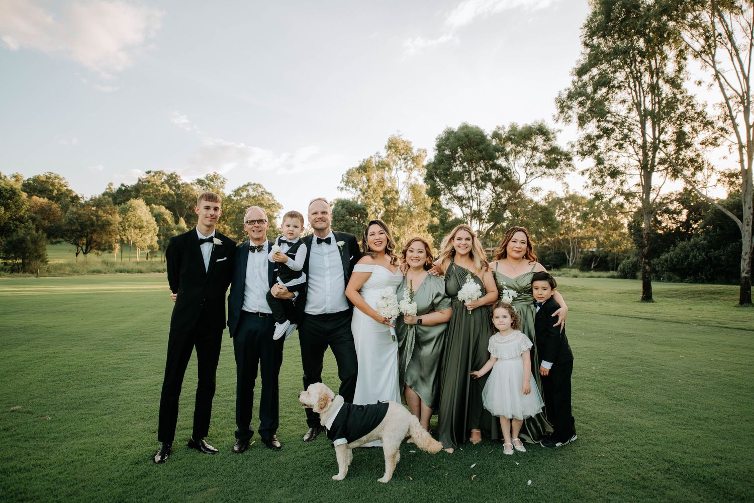 Wedding party poses on a grassy field with a happy dog joining the group photo.