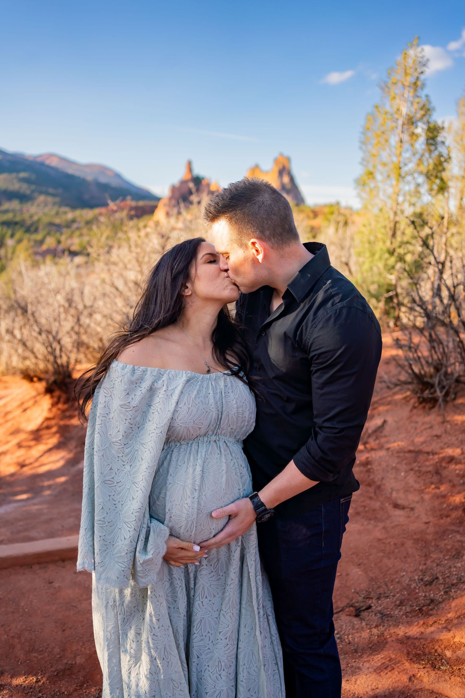 Intimate maternity moment captured against red rock formations in natural desert setting.