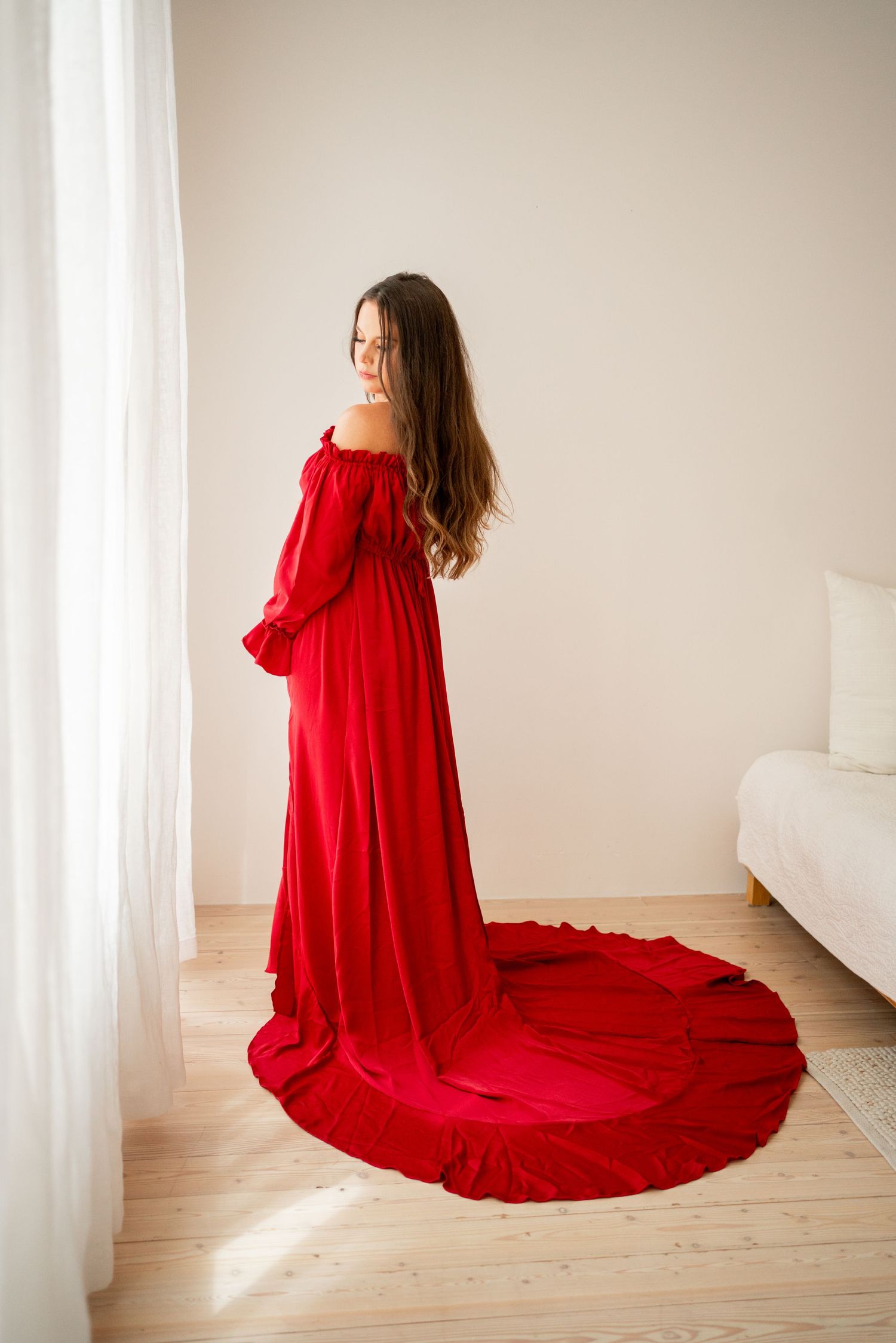 Long red dress with dramatic train photographed in a bright minimalist indoor setting.