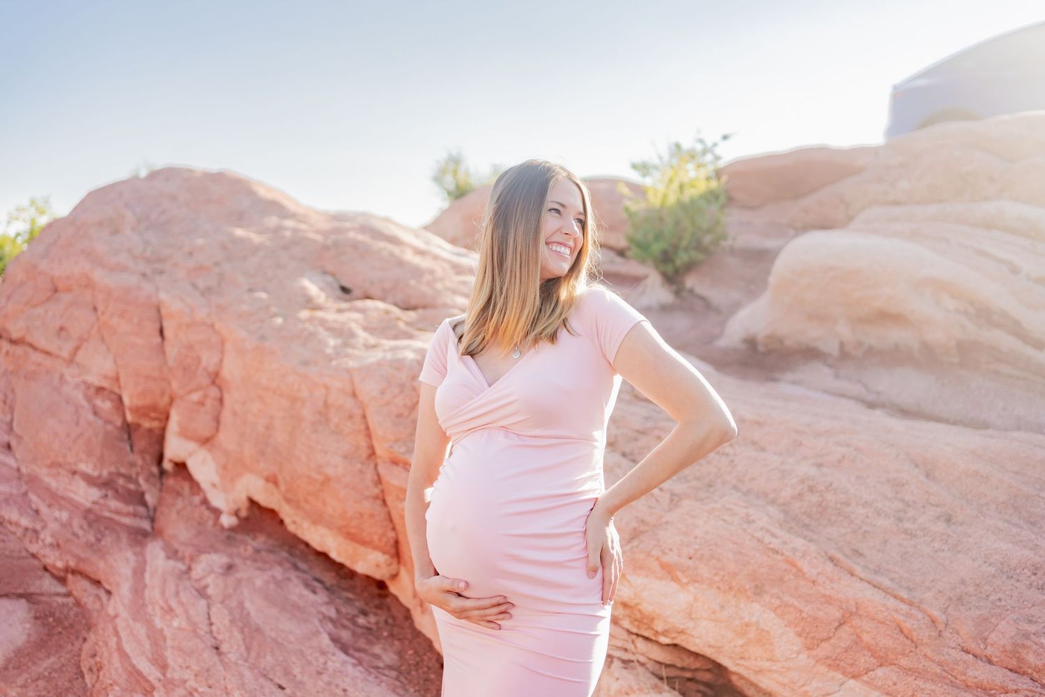 Sunset maternity portrait in pink dress against red rock landscape.
