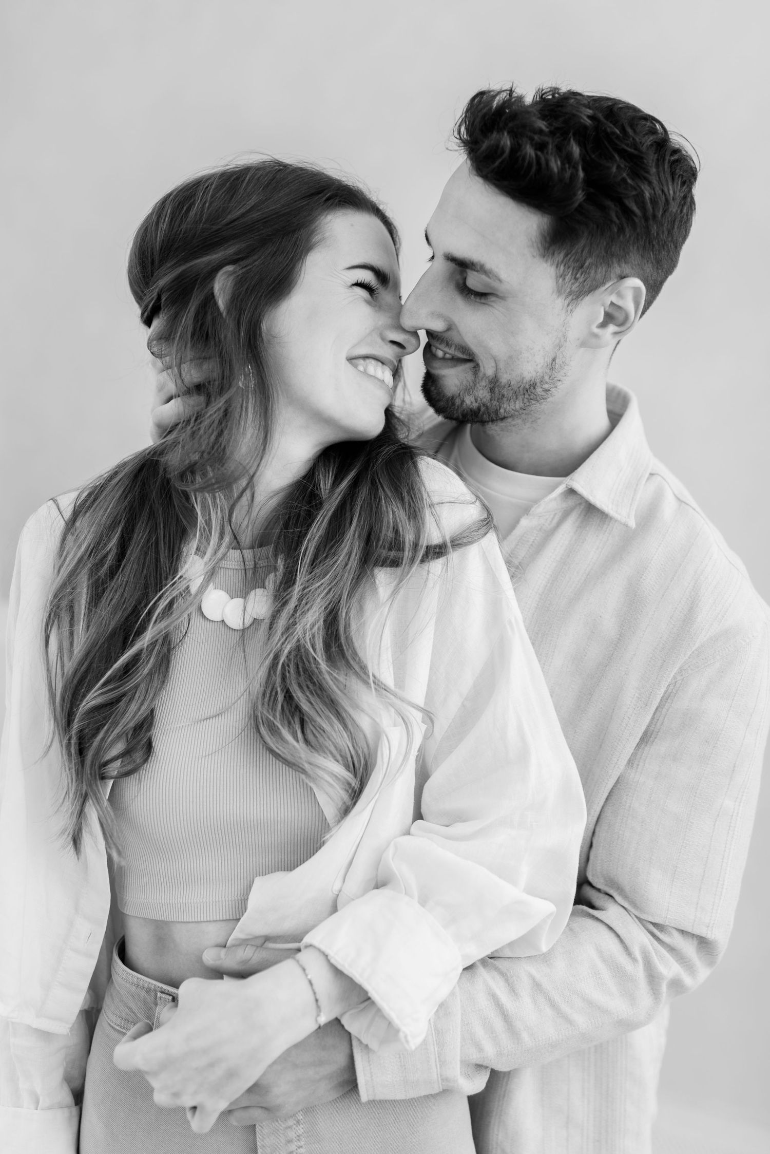 Romantic black and white portrait of a couple in white clothing embracing and smiling intimately.