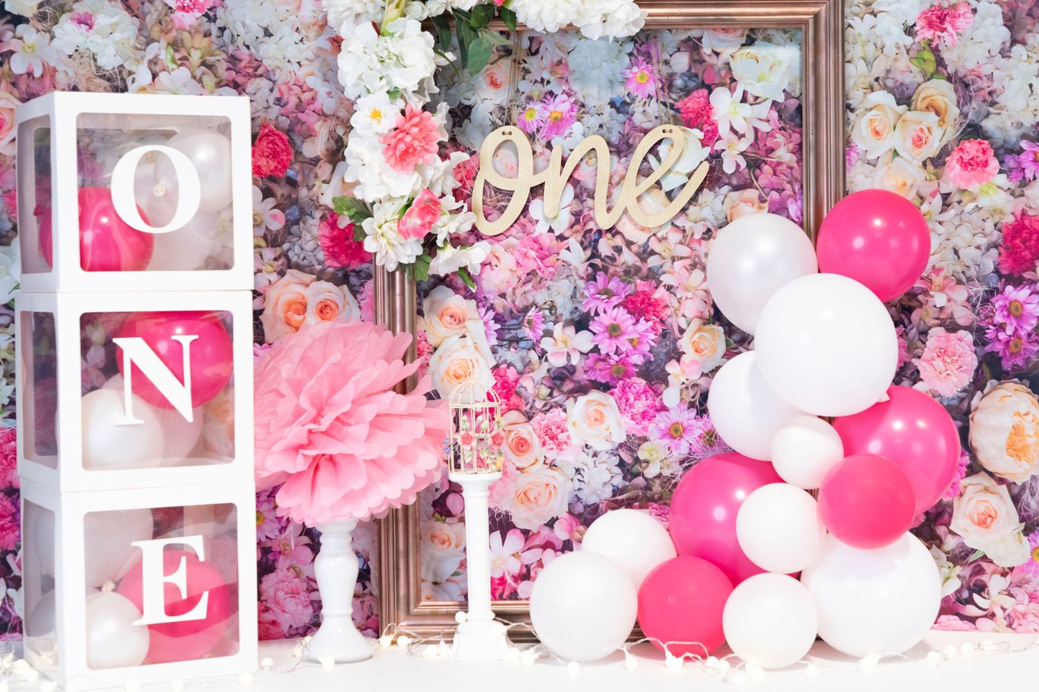 Pink and white floral birthday backdrop with ONE blocks and balloon decorations.